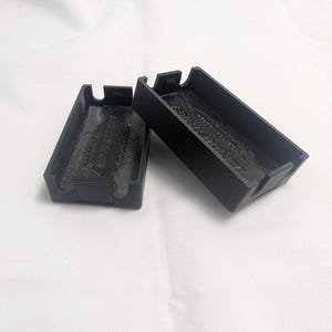 May include: Two black rectangular cases with a textured interior and a small tab on each end. The cases are made of a matte black material and are resting on a white surface. The text "INDUSTRIES" is visible on the interior of one case.