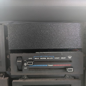 May include: A black car dashboard with a control panel for the air conditioning system. The panel has buttons for "Off", "Max", "Norm", "Bi-Lev", "Vent", and "Heat". There is a knob for temperature control and a knob for fan speed.