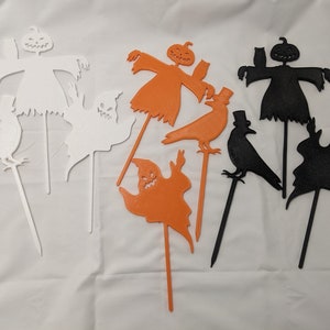 May include: Set of eight Halloween yard decorations, including a ghost, a crow, and a scarecrow. The decorations are made of white, black, and orange cardboard and are attached to sticks.