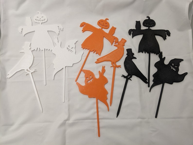 May include: Set of eight Halloween yard decorations, including a ghost, a crow, and a scarecrow. The decorations are made of white, black, and orange cardboard and are attached to sticks.