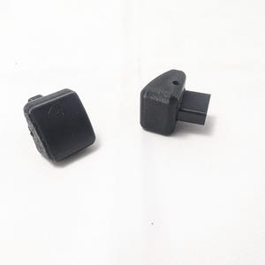 May include: Two black plastic plugs, one with a rectangular shape and the other with a rectangular shape and a small protruding piece.