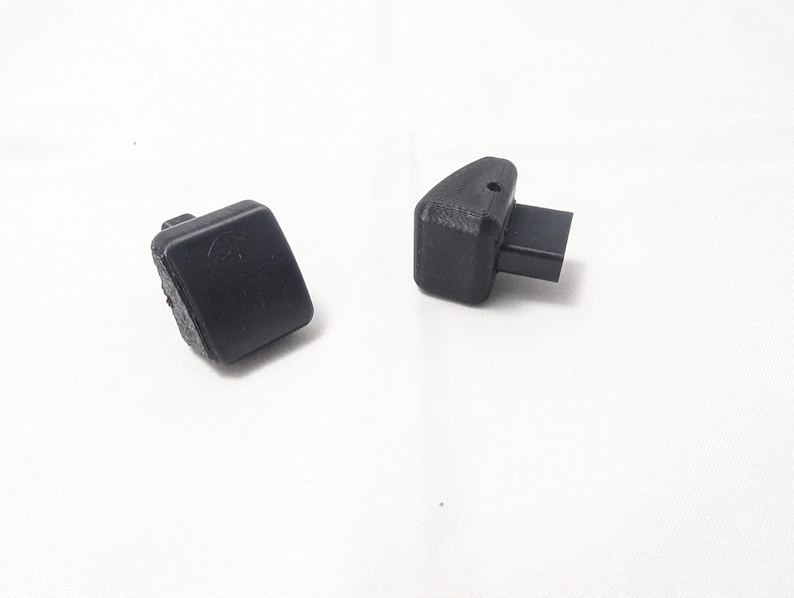 May include: Two black plastic plugs, one with a rectangular shape and the other with a rectangular shape and a small protruding piece.