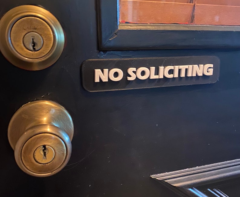 May include: A black door with a gold door knob and a sign that reads "NO SOLICITING" in white letters.