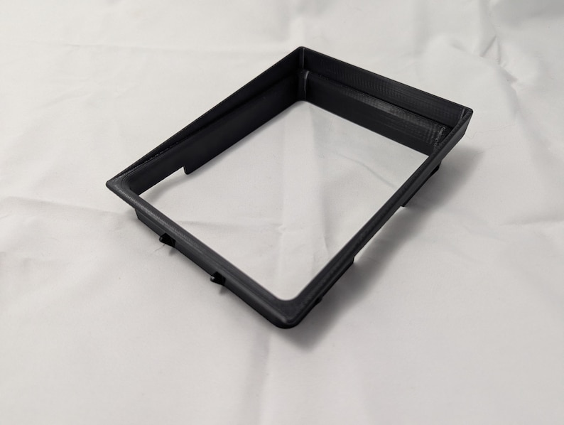 May include: A black plastic frame with a rectangular opening. The frame is made of 3D printed plastic.