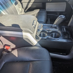 May include: The interior of a car with black leather seats, a centre console with two cup holders, and a gear shifter. The console is made of black plastic and has a silver trim.