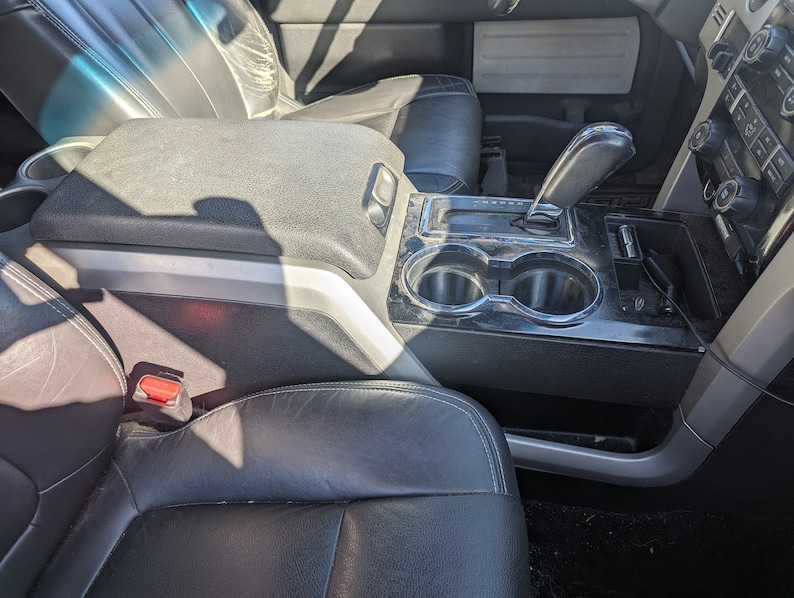 May include: The interior of a car with black leather seats, a centre console with two cup holders, and a gear shifter. The console is made of black plastic and has a silver trim.