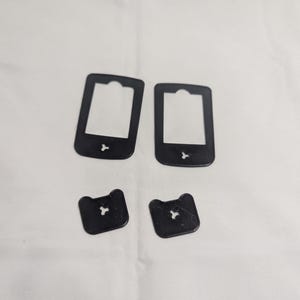 May include: Four black plastic bread bag clips and tags are arranged on a white surface. Two rectangular tags have a cutout at the top and a small shape at the bottom. Two smaller, square-shaped clips have a star-shaped cutout.