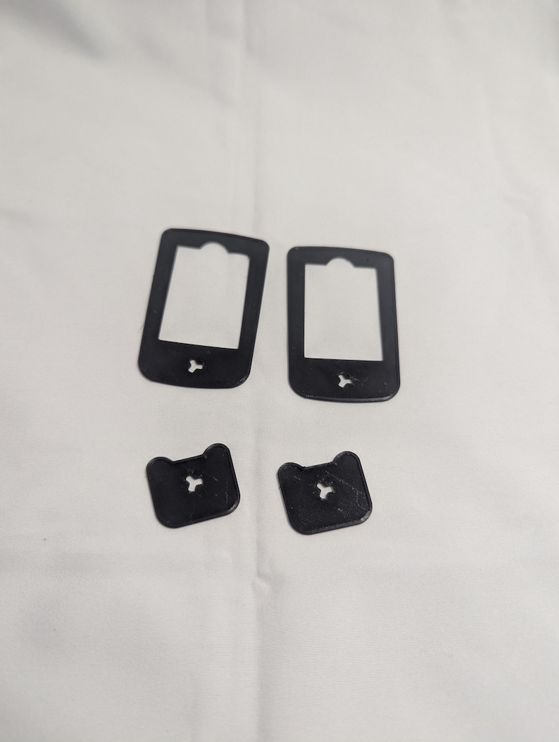 May include: Four black plastic bread bag clips and tags are arranged on a white surface. Two rectangular tags have a cutout at the top and a small shape at the bottom. Two smaller, square-shaped clips have a star-shaped cutout.