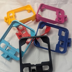 May include: A collection of colorful 3D-printed phone cases in various colors, including yellow, pink, blue, red, and black. The cases have a rectangular shape with cutouts for buttons and a camera.