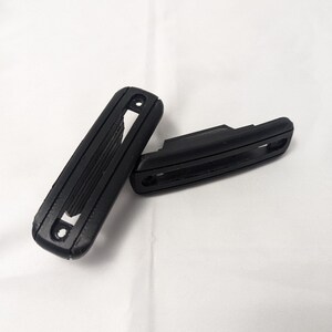 May include: Two black plastic car door handles with a textured surface and a rectangular shape.