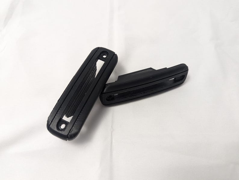 May include: Two black plastic car door handles with a textured surface and a rectangular shape.