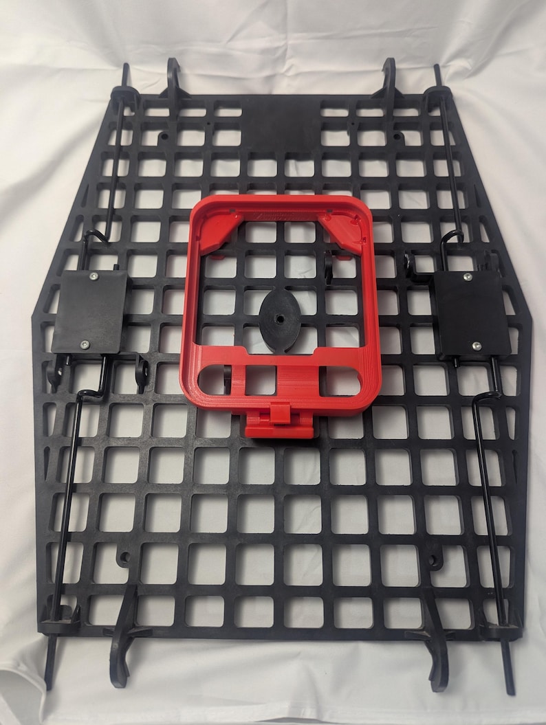 May include: Black, square-patterned panel with a red rectangular frame and black components. The panel has a grid-like design with numerous square openings. The red frame is centered on the panel, and black components are attached to the sides.