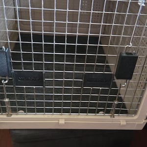 May include: A cream-colored pet carrier with a metal wire door and top. The carrier has a black floor and black latches to secure the door. The carrier is designed for safe pet travel.