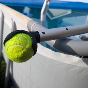 May include: A yellow tennis ball attached to a black and silver pool cleaning tool. The tool is attached to the side of a blue and white above ground pool.