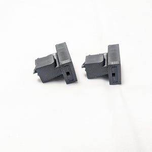 May include: Two black plastic 3D printed parts with a rectangular shape and a small hole in the center.