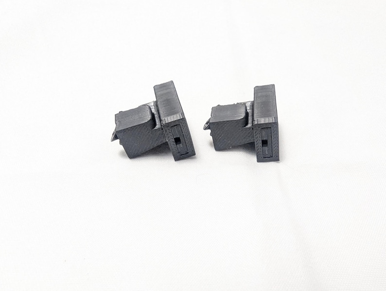 May include: Two black plastic 3D printed parts with a rectangular shape and a small hole in the center.