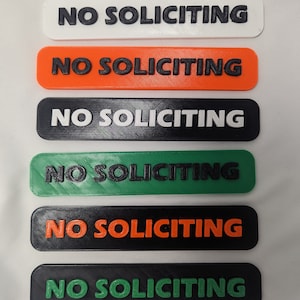 May include: Six different color variations of a "No Soliciting" sign. The signs are rectangular and have a raised, black, 3D printed font.