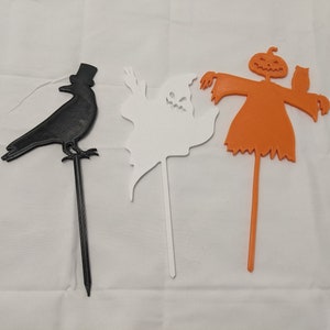 May include: Three Halloween yard decorations: a black crow with a top hat, a white ghost, and an orange scarecrow with a pumpkin head and an owl.
