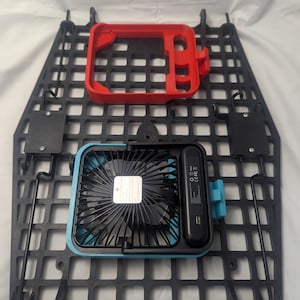 May include: A black plastic grid with a red frame and a blue and black fan. The fan has a USB port and a small label. The grid has several mounting brackets.