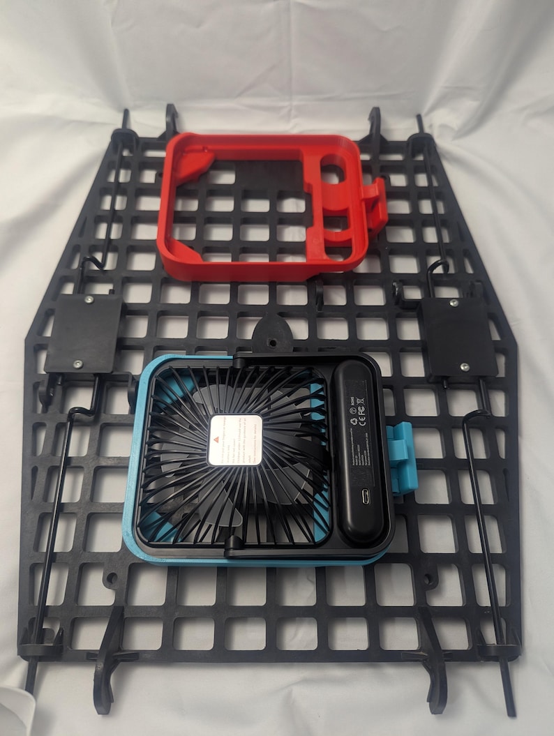 May include: A black plastic grid with a red frame and a blue and black fan. The fan has a USB port and a small label. The grid has several mounting brackets.