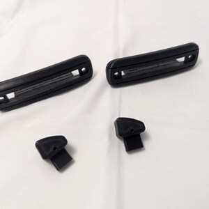 May include: Four black plastic pieces, two long rectangular pieces with a groove in the center, and two smaller pieces with a rounded top and a flat bottom.
