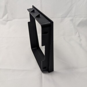 May include: Black plastic frame with a square opening. The frame is designed to be mounted on a wall.