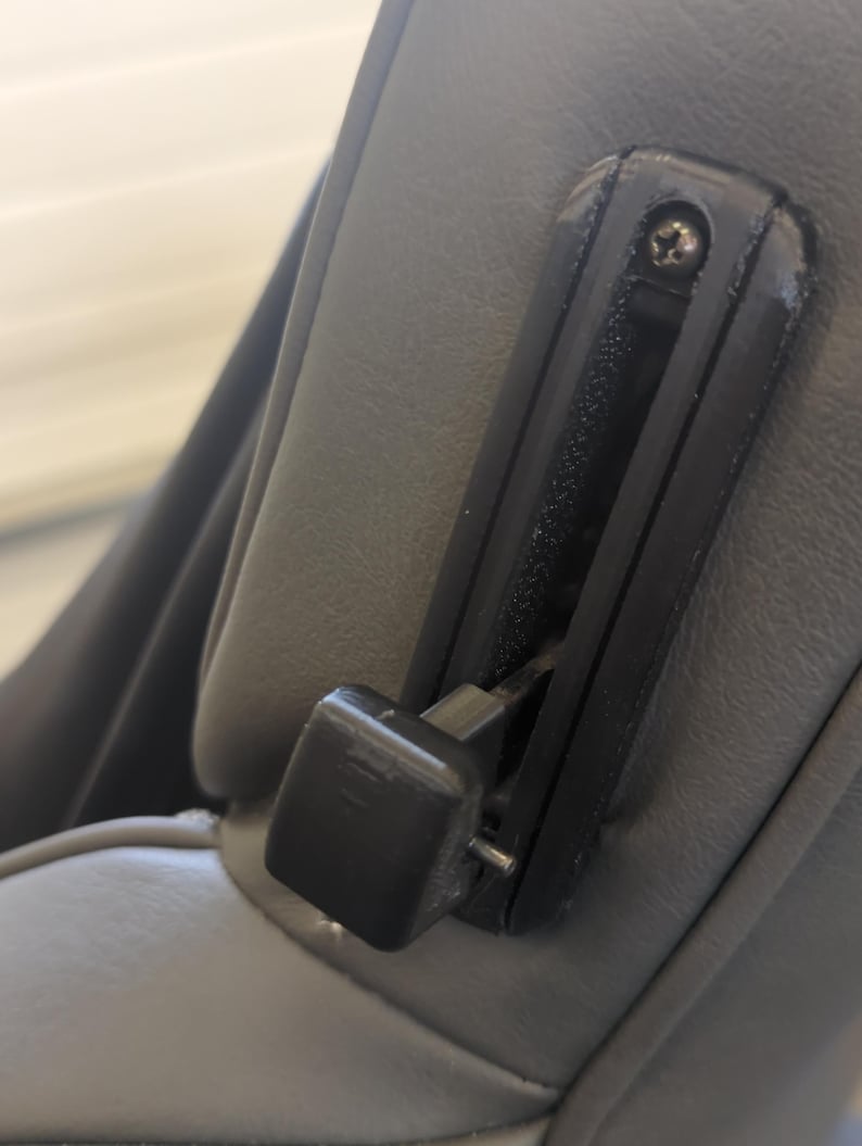 May include: A black plastic lever with a gray fabric background. The lever is attached to a gray fabric seat.