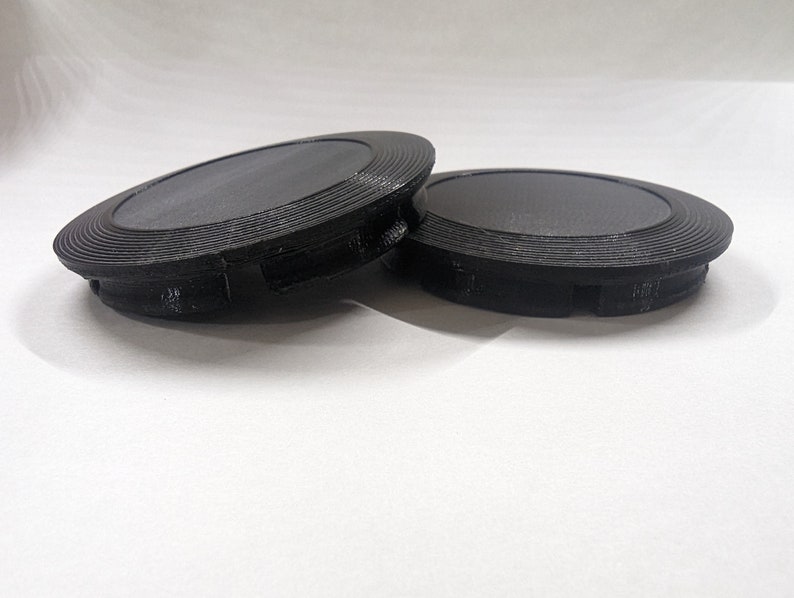 May include: Two black plastic round covers with a textured surface and a raised lip around the edge.