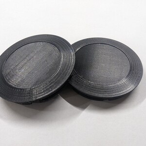 May include: Two black plastic round lids with a concentric circle design.