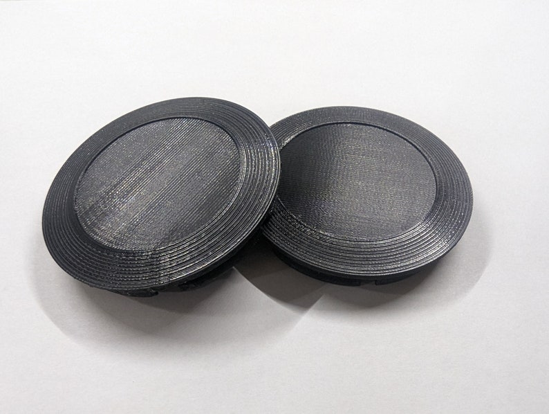 May include: Two black plastic round lids with a concentric circle design.