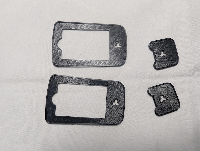 May include: Four black, 3D-printed plastic parts. Two rectangular frames with a cutout on one side and a small, three-pronged hole. Two smaller, square-shaped pieces with a similar three-pronged hole.