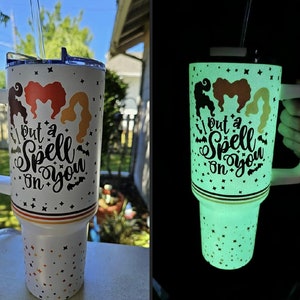 May include: A white tumbler with a black and gold design featuring three witches and the text "I put a spell on you". The tumbler glows in the dark.