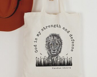 May include: A white canvas tote bag with a black and white illustration of a lion and the text "God is my strength and defense Exodus 15:1-4".