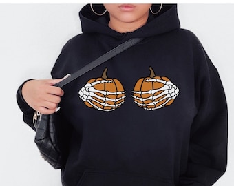 Peut inclure: Sweat-shirt noir avec un motif de deux citrouilles orange avec des mains squelettiques blanches.