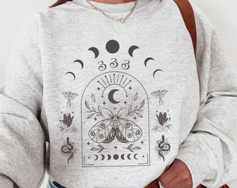May include: A gray sweatshirt with a graphic print of a moth, moon phases, and the number 333. The graphic is in a black and white color scheme.