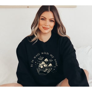 May include: Black sweatshirt with a graphic design of a skull with mushrooms and butterflies. The text "It is well with my soul" is printed around the skull.