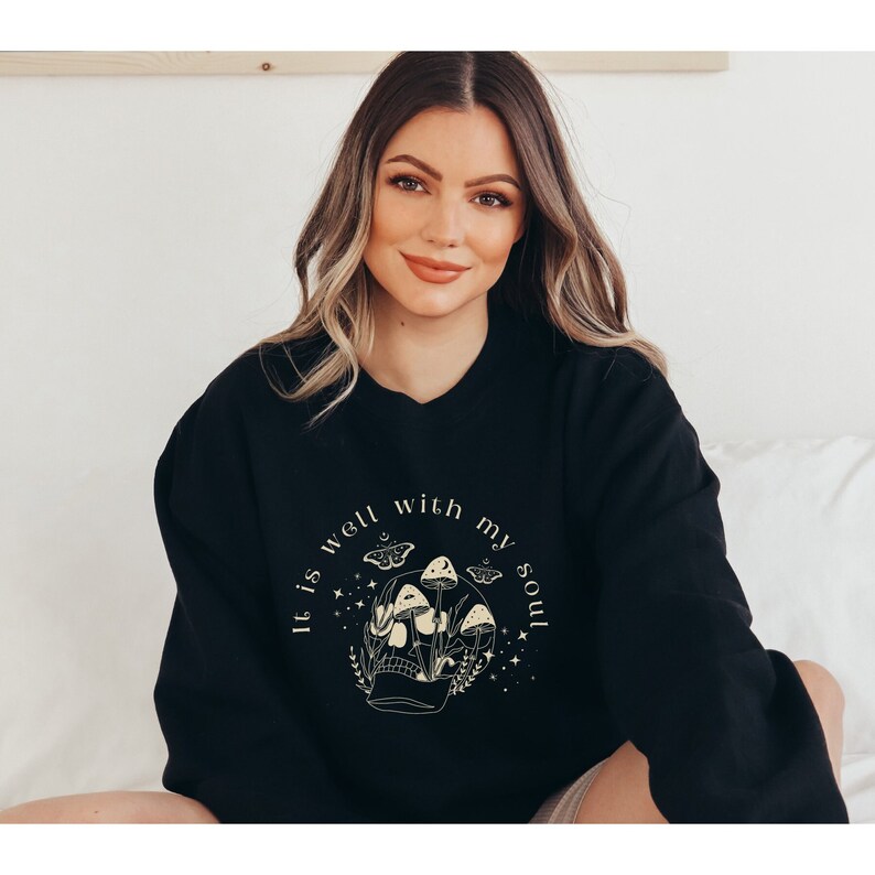 May include: Black sweatshirt with a graphic design of a skull with mushrooms and butterflies. The text "It is well with my soul" is printed around the skull.
