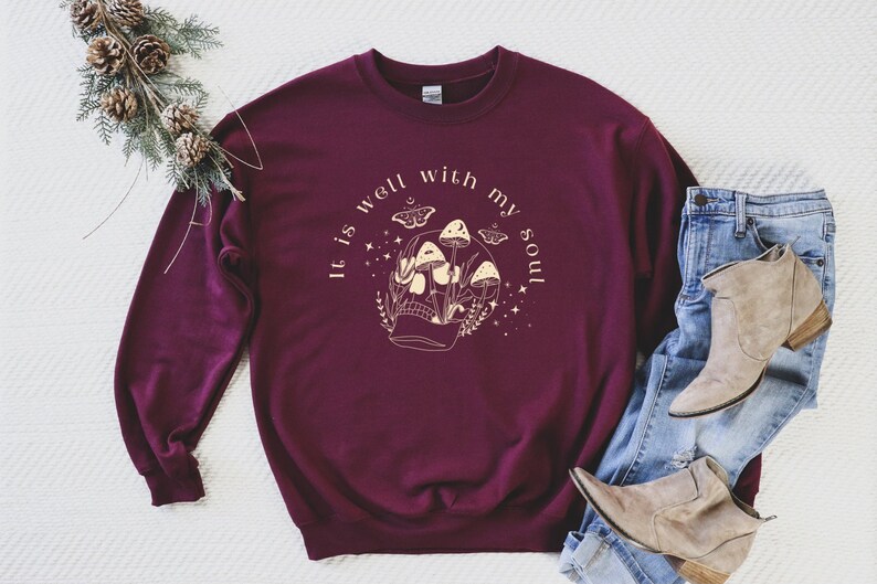 May include: Burgundy sweatshirt with a graphic of a skull with mushrooms growing out of it. The text "It is well with my soul" is printed around the graphic.