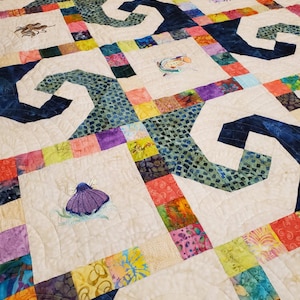 May include: A quilt with a patchwork design featuring a variety of colors and patterns. The quilt is made up of squares and rectangles, and the fabric is a mix of cotton and silk. The quilt is decorated with embroidered sea creatures, including an octopus, a fish, and a seashell.