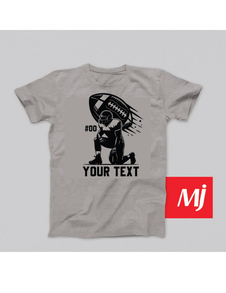 K&ouml;nnte beinhalten: Ein graues T-Shirt mit einer schwarzen Illustration eines Fussballspielers, der kniet und einen Fussball in der Luft h&auml;lt. Der Text "#00" und "YOUR TEXT" ist auf dem T-Shirt aufgedruckt.