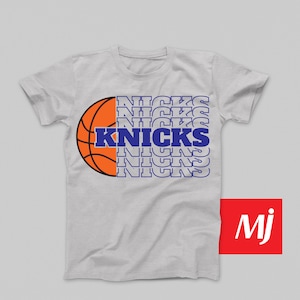 May include: A gray t-shirt with a basketball graphic and the word "KNICKS" repeated in a stacked pattern. The basketball is orange and the text is blue.
