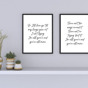May include: Two black framed prints with white backgrounds and black calligraphy text. The text on the left print reads "So I'll love ya til my lungs give out I ain't lying Im all your'n and you're all mine". The text on the right print reads "There ain't two ways around it There ain't no trying 'bout it Im all you'n and you're all mine".