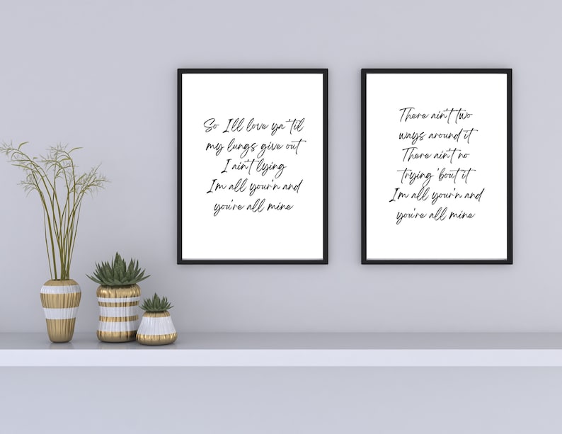 May include: Two black framed prints with white backgrounds and black calligraphy text. The text on the left print reads "So I'll love ya til my lungs give out I ain't lying Im all your'n and you're all mine". The text on the right print reads "There ain't two ways around it There ain't no trying 'bout it Im all you'n and you're all mine".