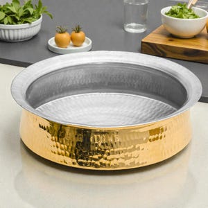 May include: A hammered metal serving bowl with a gold-colored base and a silver-colored rim. The bowl has a wide, shallow design, suitable for serving dishes. The interior has a textured, dimpled surface.