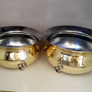 Puede incluir: Dos cuencos de metal de color dorado con interiores de plata martillados. Los cuencos son redondos y tienen una base ancha y plana.