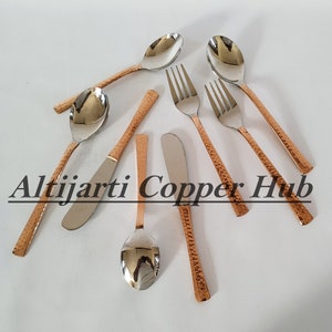 May include: Set of copper and stainless steel cutlery, including spoons, forks, and a butter knife. The handles have a hammered copper finish.