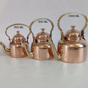 May include: Three copper teapots with brass handles and spouts. The teapots are labeled with their capacity: 300 ml, 500 ml, and 1000 ml. The copper has a hammered texture, and the handles arch over the lids.