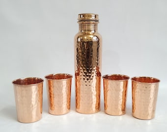 May include: Set of five copper hammered drinking glasses and a copper water bottle. The glasses and bottle have a hammered texture and are a shiny copper color.