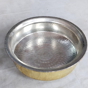 May include: A hammered metal bowl with a silver interior and a gold-coloured exterior. The bowl has a wide, shallow design with a slightly raised rim. The metal surface has a textured, dimpled appearance.
