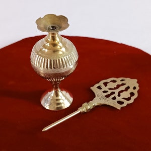 May include: A gold metal oil dispenser with a decorative top and a matching ornate metal applicator. The dispenser is sitting on a red velvet surface.